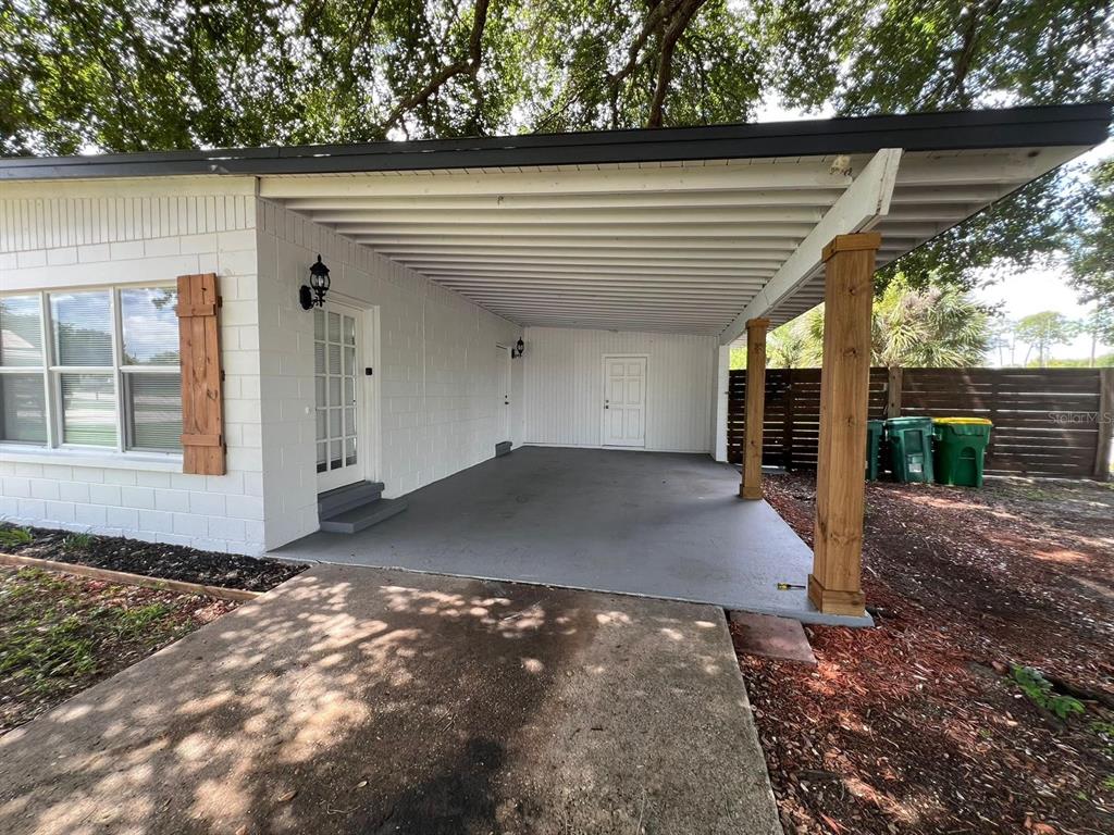 A white concrete block house features a covered carport with wooden support posts — 1221 CYPRESS LANE, COCOA, FL