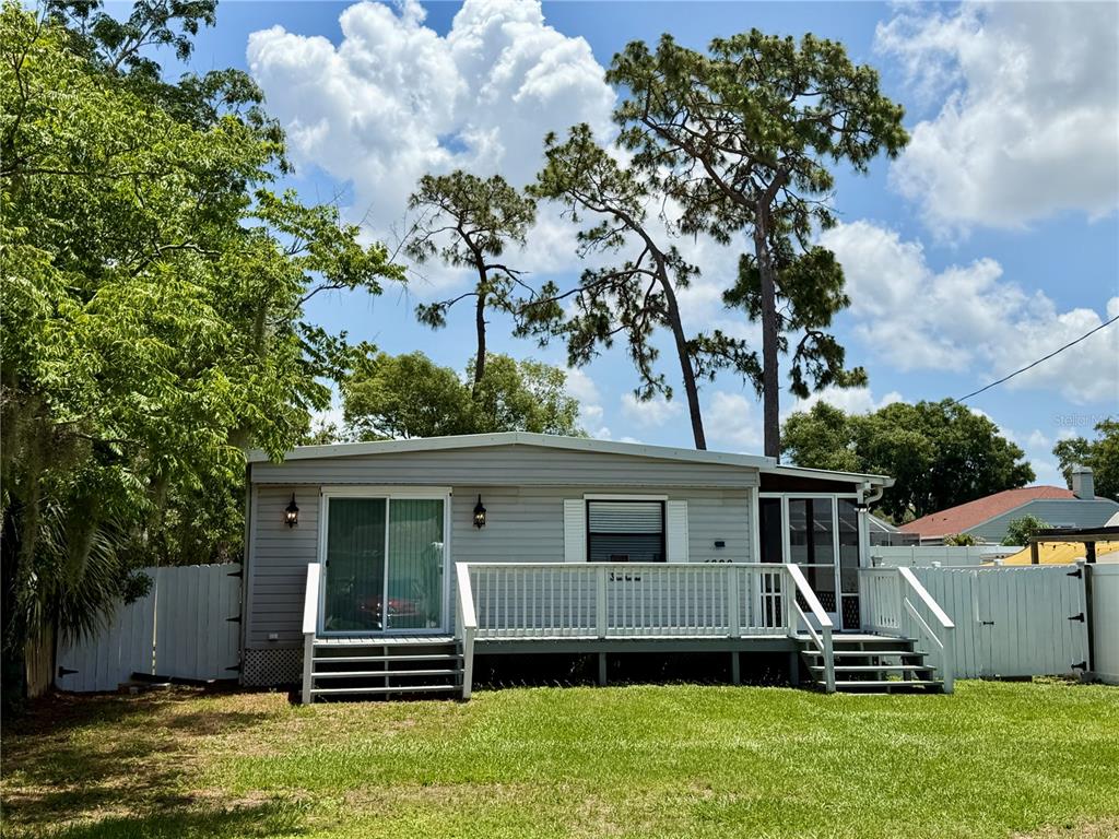 A light gray mobile home features a wooden deck with white railings and stairs — 4820 CAPRON STREET, NEW PORT RICHEY, FL