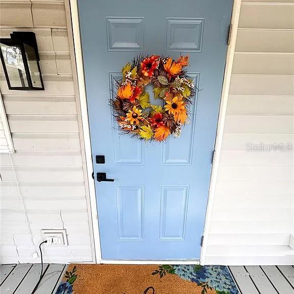 A light blue front door with a fall wreath is set against white horizontal siding — 4820 CAPRON STREET, NEW PORT RICHEY, FL