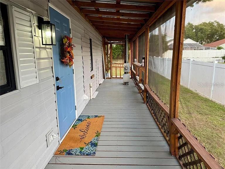 A covered wooden porch features a blue front door, a welcome mat, and screened walls — 4820 CAPRON STREET, NEW PORT RICHEY, FL