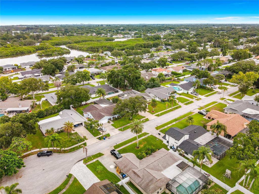 An aerial view shows a residential neighborhood with single-family homes, green lawns, and nearby waterways — 1855 DEL ROBLES TERRACE, CLEARWATER, FL