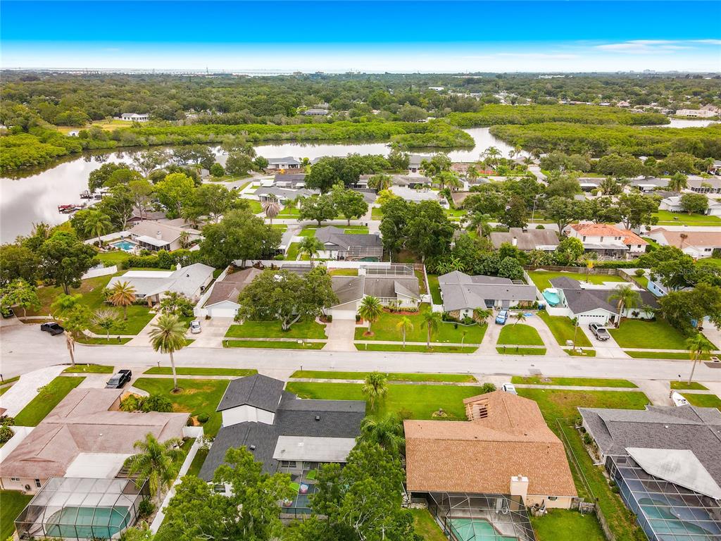 An aerial view shows a suburban neighborhood with houses, swimming pools, and surrounding green space — 1855 DEL ROBLES TERRACE, CLEARWATER, FL