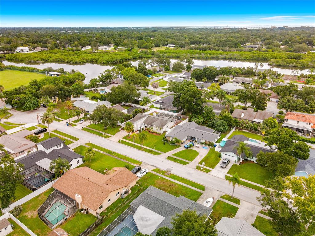 An aerial view shows a suburban neighborhood with houses, swimming pools, and a nearby waterway — 1855 DEL ROBLES TERRACE, CLEARWATER, FL
