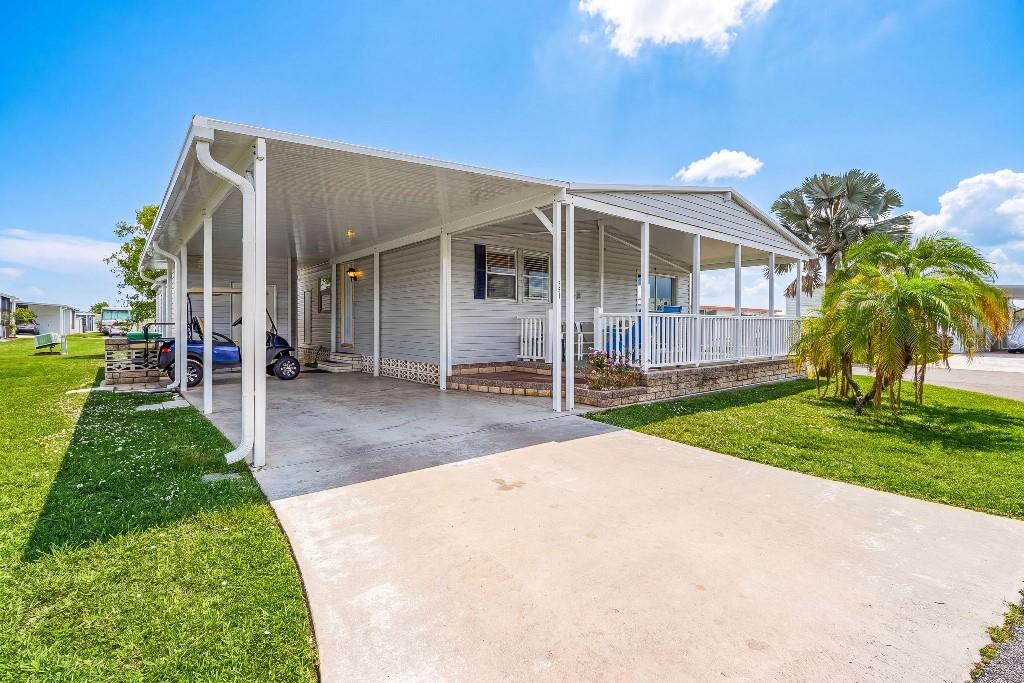 A single-story manufactured home features a concrete driveway, a carport, and a screened-in front porch — 251 IBIS, PUNTA GORDA, FL