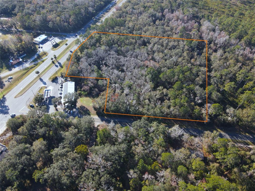 An aerial view shows a wooded lot outlined in orange next to a commercial property — 102 NE HIGHWAY 441, MICANOPY, FL
