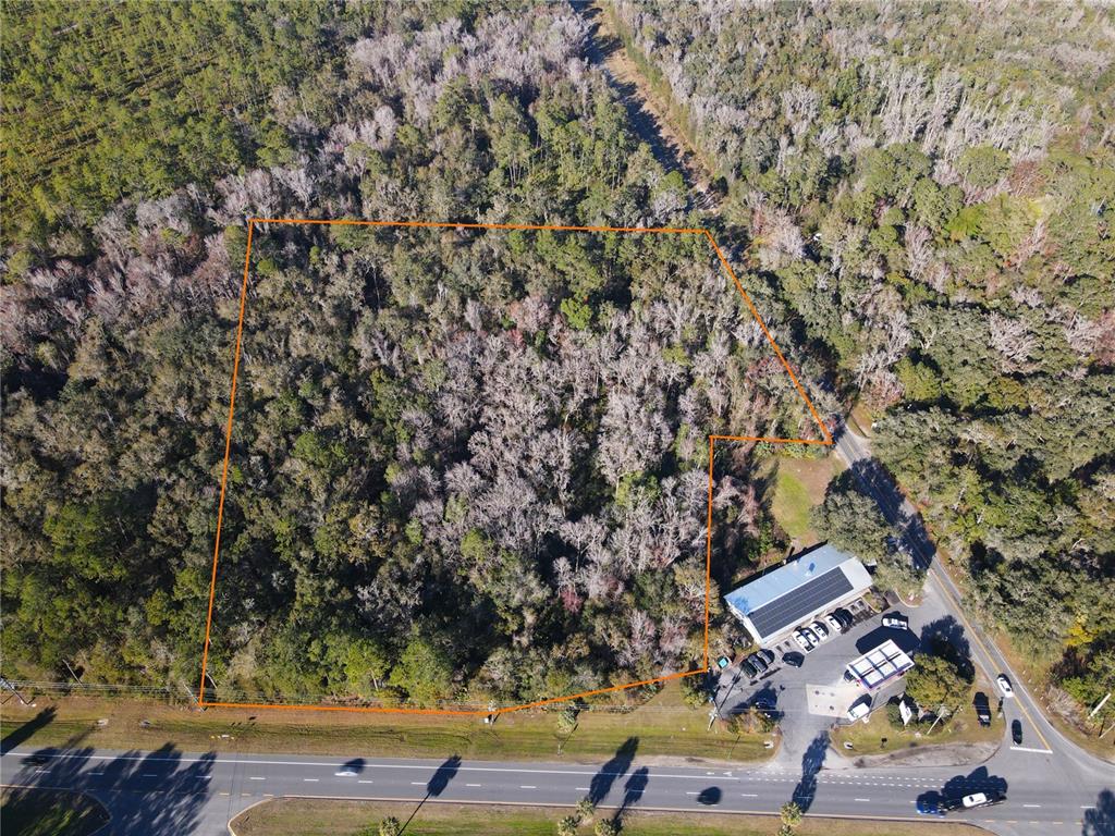 An aerial view shows a wooded lot outlined in orange next to a commercial building — 102 NE HIGHWAY 441, MICANOPY, FL