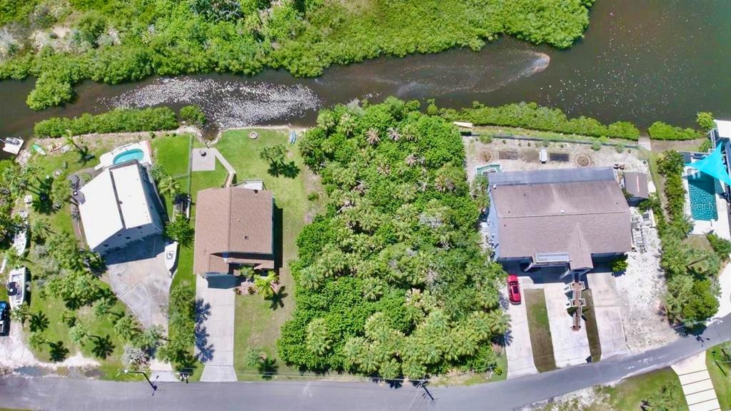 An aerial view shows three houses along a waterway with lush vegetation and private pools — WELLS COURT, PORT RICHEY, FL