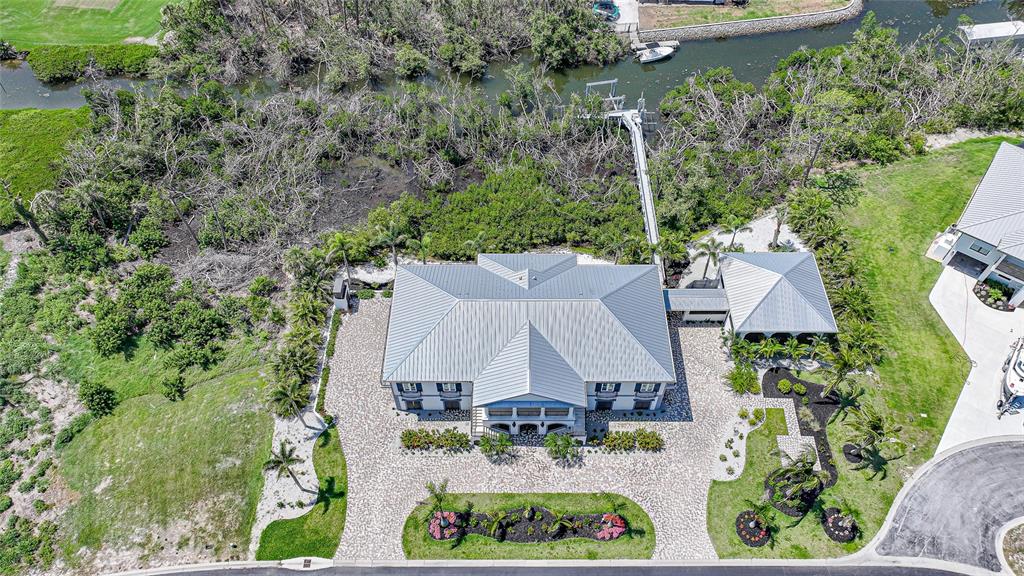An aerial view shows a large house with a metal roof, paved driveway, and dock — 10161 EAGLE PRESERVE DRIVE, ENGLEWOOD, FL