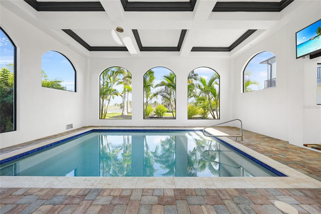 An indoor swimming pool room features arched windows, a coffered ceiling, and stone paver flooring — 10161 EAGLE PRESERVE DRIVE, ENGLEWOOD, FL