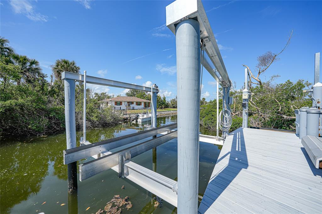 A boat lift with metal beams extends over a canal next to a wooden dock — 10161 EAGLE PRESERVE DRIVE, ENGLEWOOD, FL