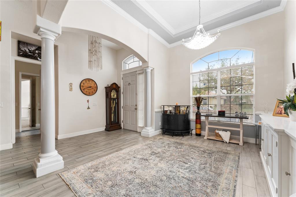 A bright foyer features gray wood-look tile flooring, a grand chandelier, and a grandfather clock — 2770 SWOOP CIRCLE, KISSIMMEE, FL