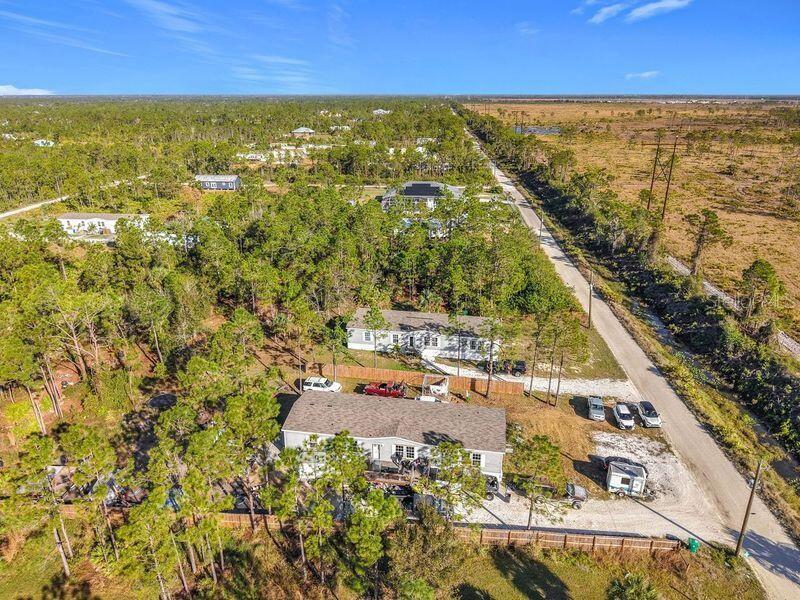 An aerial view shows two houses surrounded by trees next to a dirt road — 8325 STRASSE BOULEVARD, PUNTA GORDA, FL