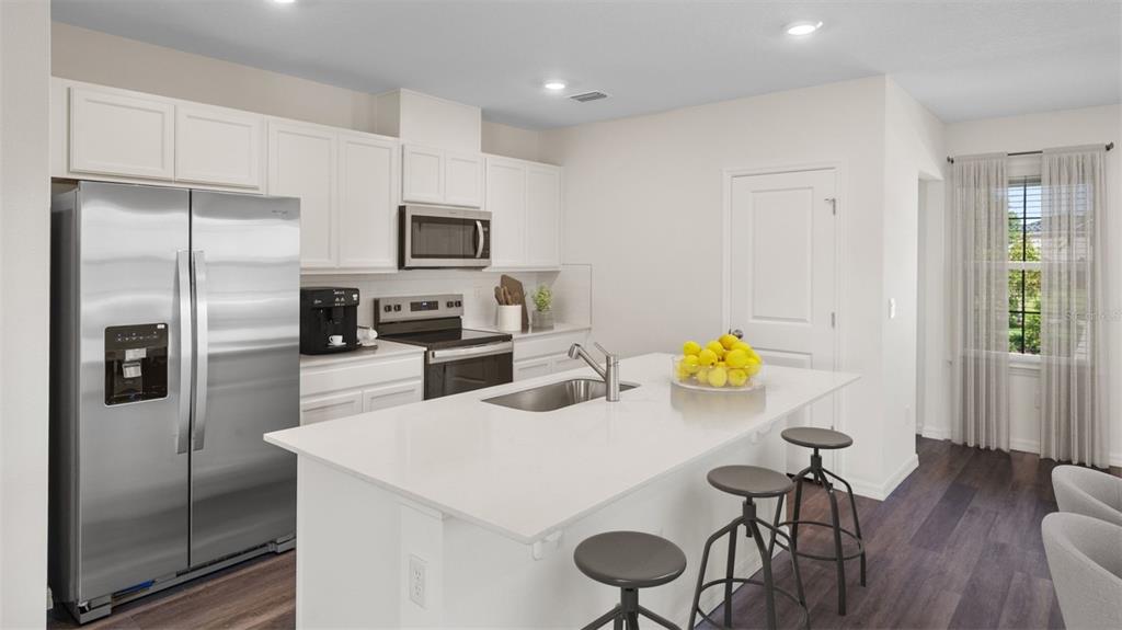 A modern kitchen features white cabinets, stainless steel appliances, a quartz island, and dark flooring — 16534 BARBOURS CREEK WAY, WINTER GARDEN, FL
