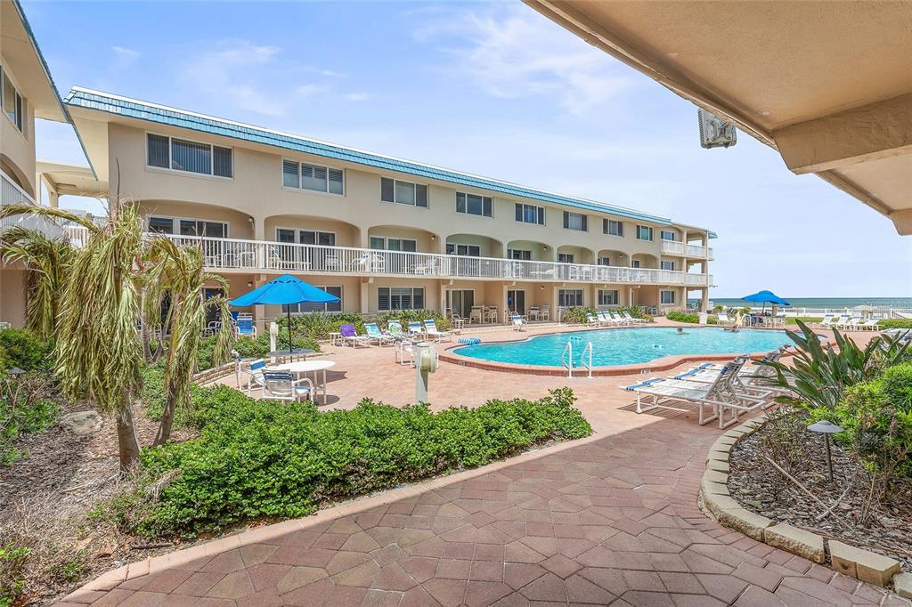 A multi-story building overlooks a swimming pool with lounge chairs and umbrellas on a patio — 111 N ATLANTIC AVENUE UNIT A101, NEW SMYRNA BEACH, FL