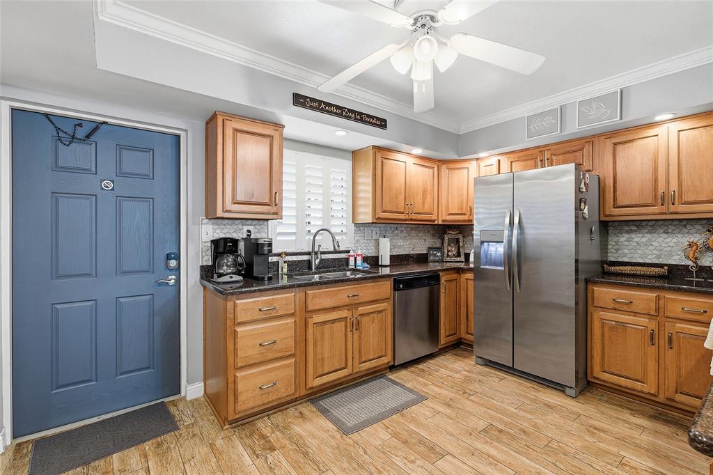 A kitchen features wood cabinets, stainless steel appliances, dark countertops, and a blue entry door — 111 N ATLANTIC AVENUE UNIT A101, NEW SMYRNA BEACH, FL