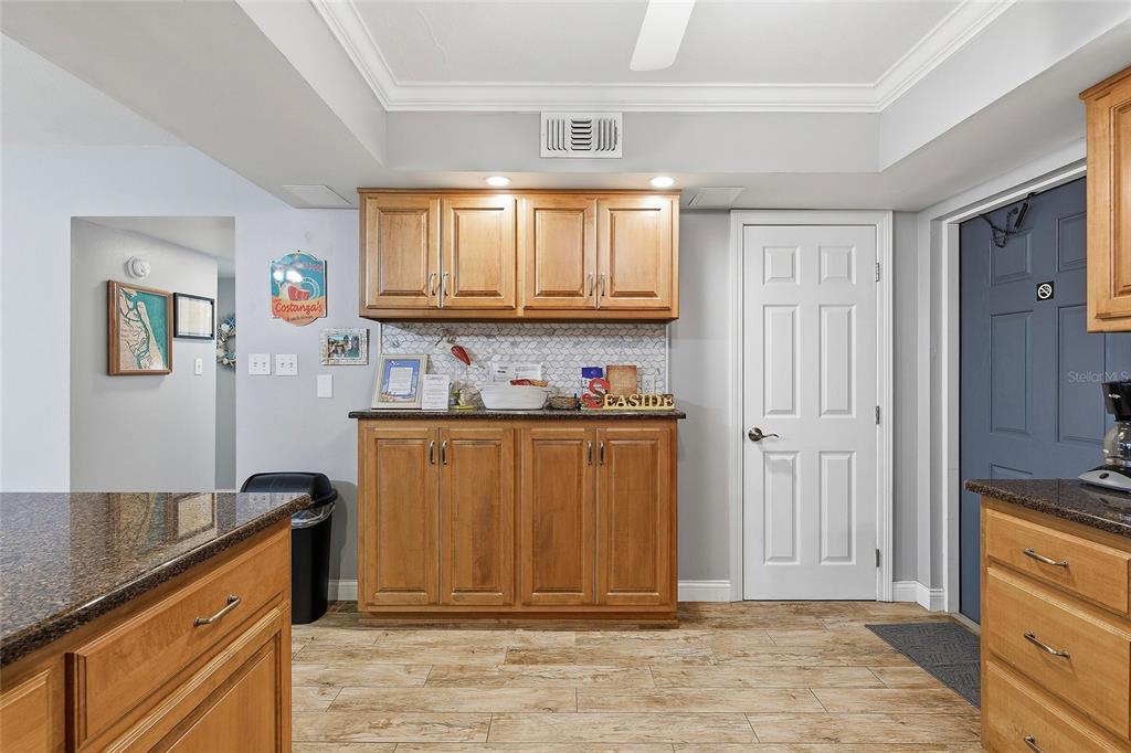 A kitchen features wood cabinets, granite countertops, a tiled backsplash, and light-colored tile flooring — 111 N ATLANTIC AVENUE UNIT A101, NEW SMYRNA BEACH, FL