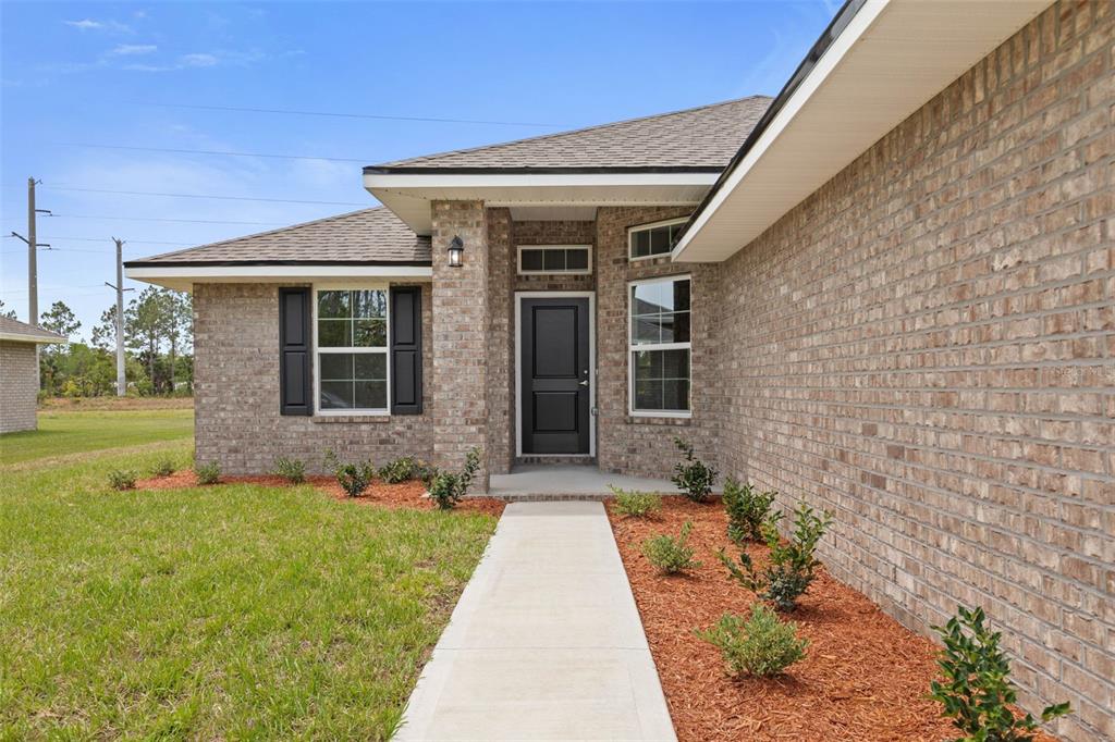 A single-story brick house with a white garage door and a concrete walkway — 47 BRUNSWICK LANE, PALM COAST, FL
