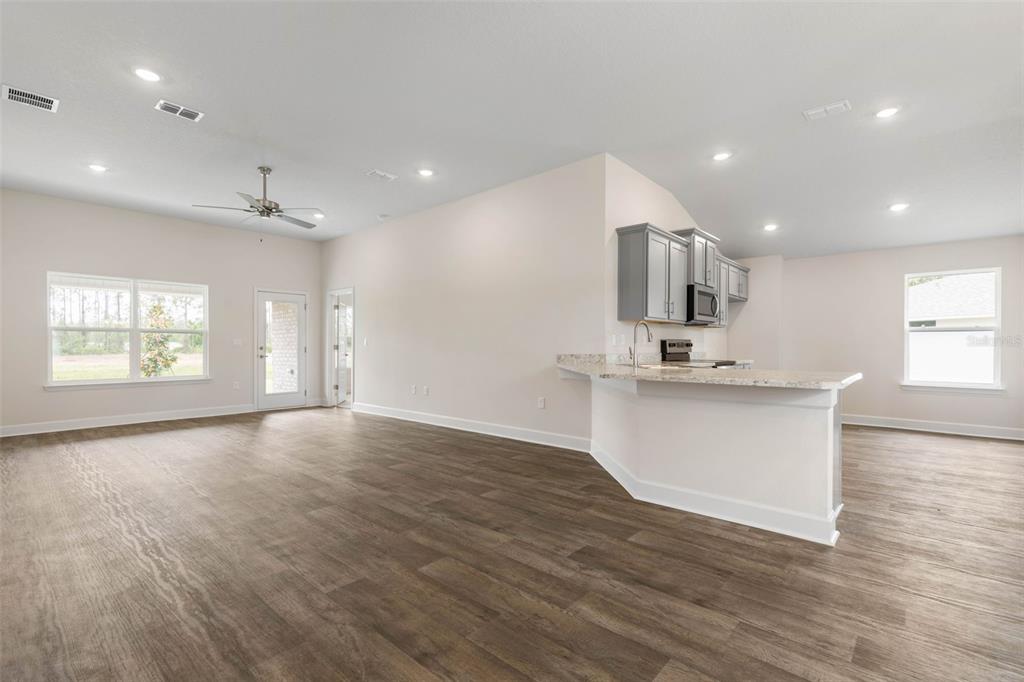 A dining area with dark wood flooring transitions to a carpeted living space and kitchen — 47 BRUNSWICK LANE, PALM COAST, FL