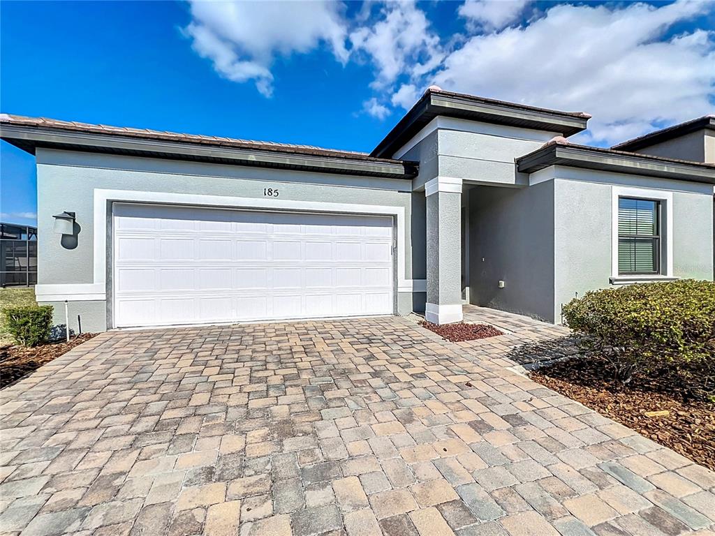 A single-story house exterior features a two-car garage, a paved driveway, and a covered entryway — 185 BROOKES PLACE, HAINES CITY, FL