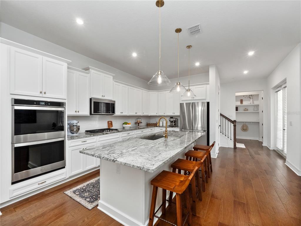 A modern kitchen features white cabinets, granite countertops, a large island, and hardwood flooring — 7484 ESTUARY LAKE LOOP, CELEBRATION, FL