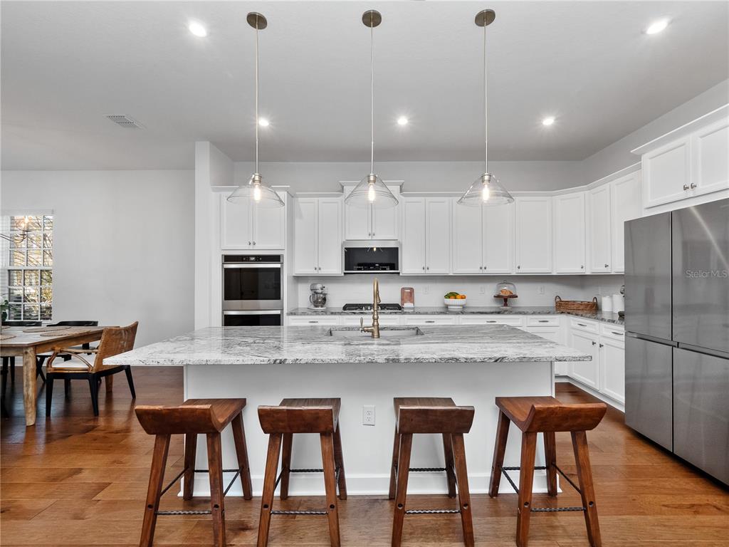 A kitchen features white cabinets, a large granite island with four wooden stools, and stainless appliances — 7484 ESTUARY LAKE LOOP, CELEBRATION, FL