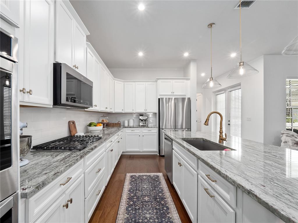 A white kitchen features granite countertops, stainless steel appliances, and a central island with seating — 7484 ESTUARY LAKE LOOP, CELEBRATION, FL