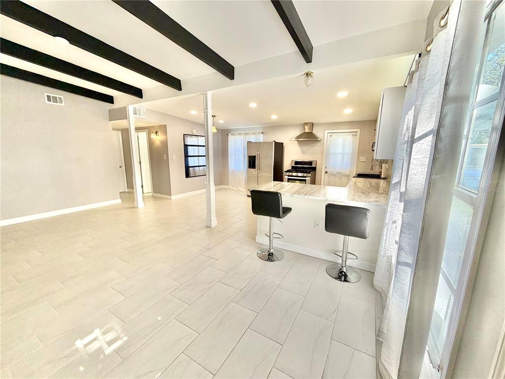 A kitchen and living area feature white tile floors, dark ceiling beams, and a breakfast bar — 1312 WINDSOR WAY, TAMPA, FL