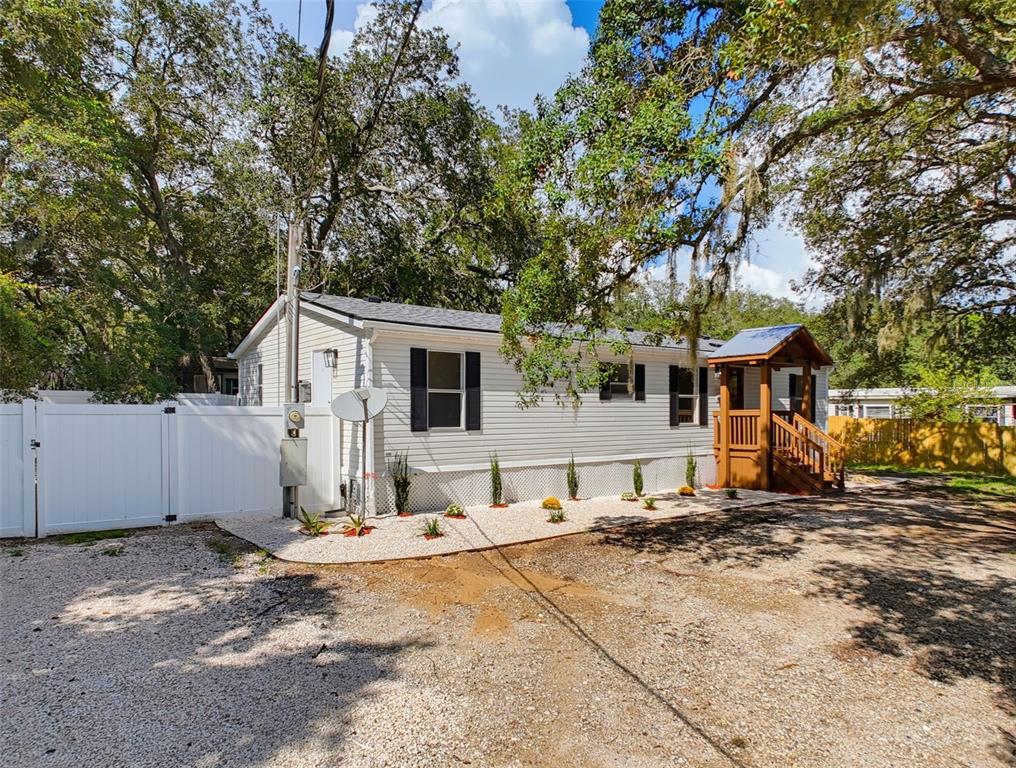 A single-story manufactured home with white siding and a wooden front porch under large trees — 9637 PASSAIC DRIVE, HUDSON, FL