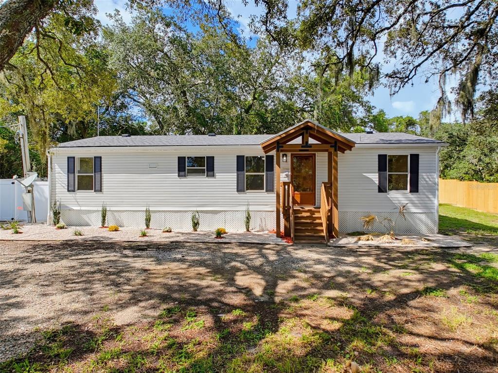 A white mobile home features a wooden front porch with stairs and dark shutters — 9637 PASSAIC DRIVE, HUDSON, FL