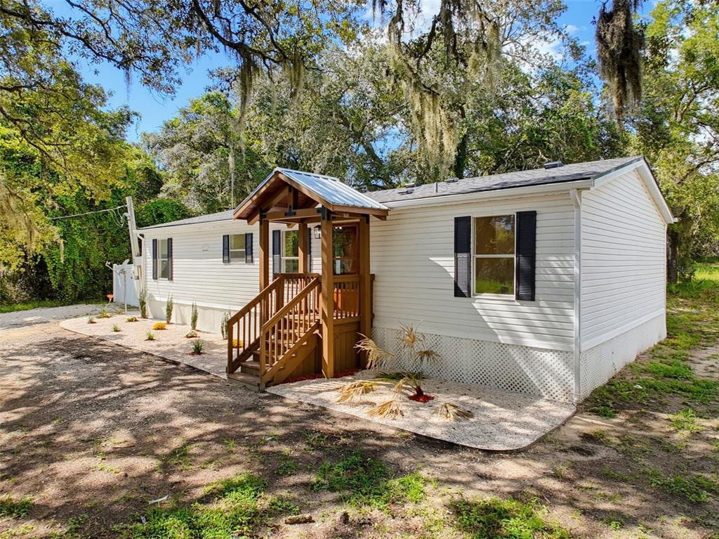 A single-story manufactured home with white siding, black shutters, and a wooden front porch — 9637 PASSAIC DRIVE, HUDSON, FL
