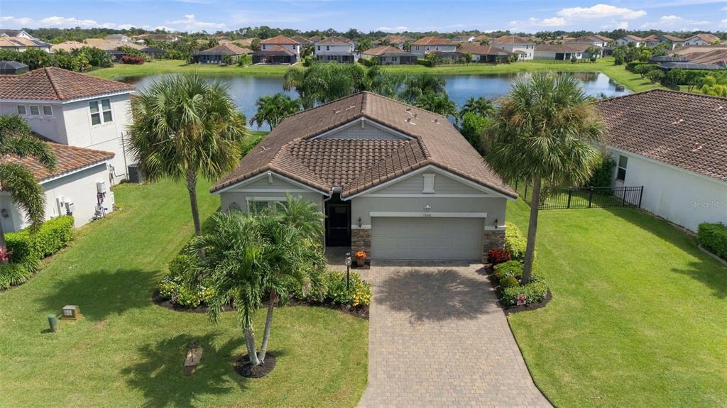 An aerial view of a single-story house with a tiled roof, driveway, and backyard lake — 13316 SAW PALM CREEK TRAIL, BRADENTON, FL