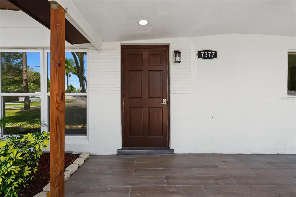 A brown front door is centered on a white brick wall under a covered porch — 7377 ROYAL PALM DRIVE, NEW PORT RICHEY, FL