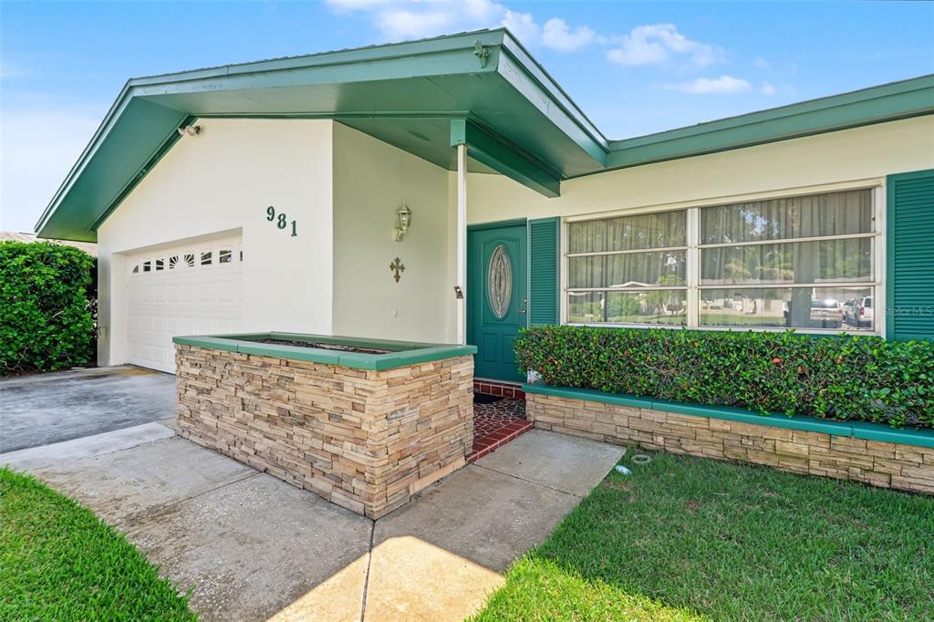 The exterior of a single-story house features a stone planter, green trim, and a garage — 981 STEPHEN FOSTER DRIVE, LARGO, FL
