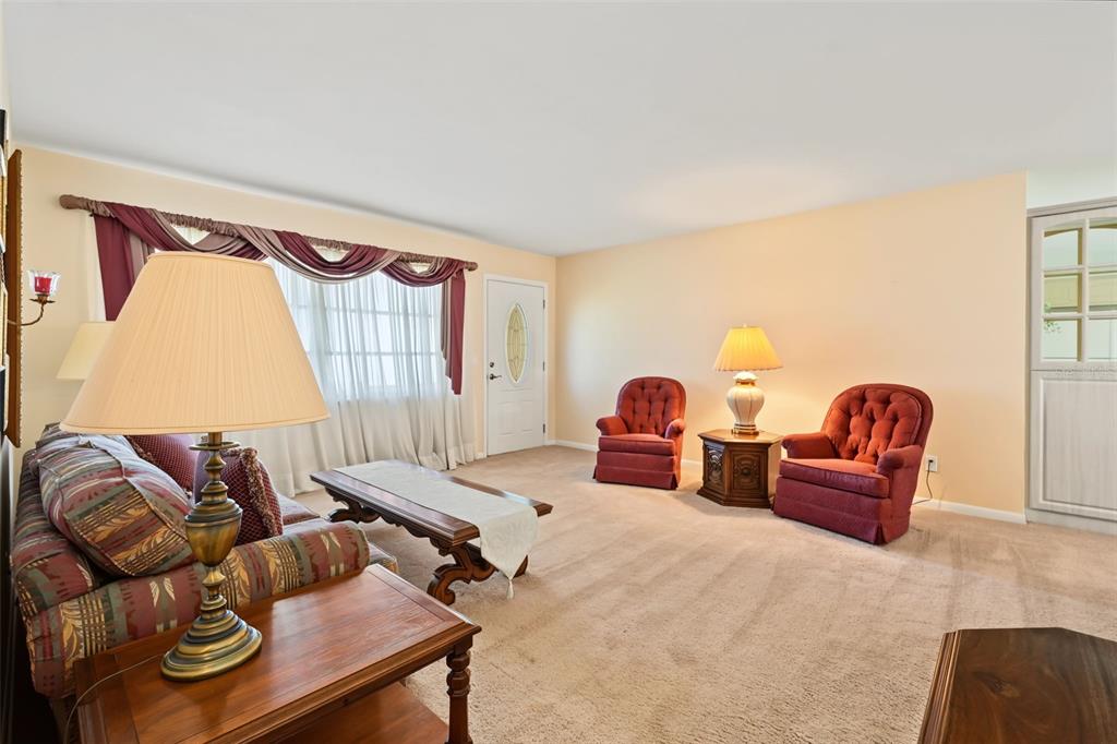 A living room features beige carpeting, a patterned sofa, two red armchairs, and a window — 981 STEPHEN FOSTER DRIVE, LARGO, FL