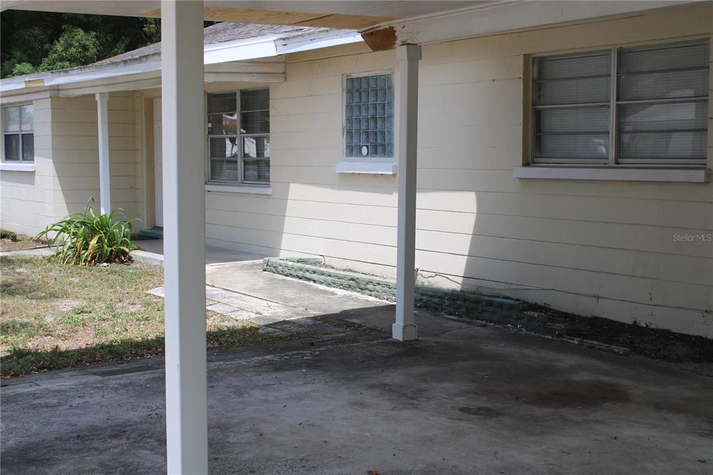A concrete carport with white support posts sits in front of a light-colored house — 2337 N CRYSTAL LAKE DRIVE, LAKELAND, FL