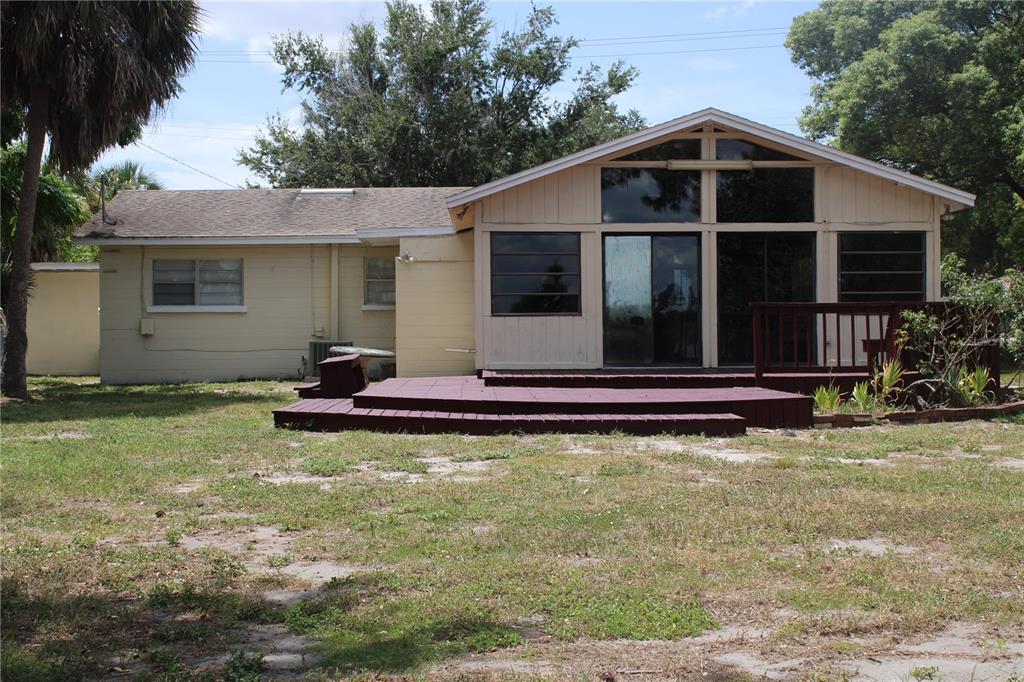 The exterior of a single-story house features light-colored siding, a dark wooden deck, and windows — 2337 N CRYSTAL LAKE DRIVE, LAKELAND, FL