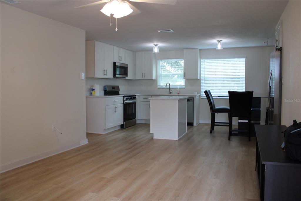 A kitchen with white cabinets, light wood-look flooring, a small island, and a dining area — 9049 ORCHID DRIVE, SEMINOLE, FL