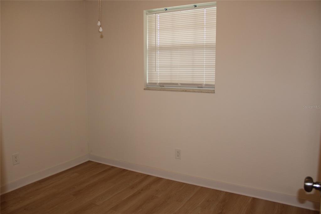 An empty room features light-colored walls, wood-look flooring, and a window with white blinds — 9049 ORCHID DRIVE, SEMINOLE, FL