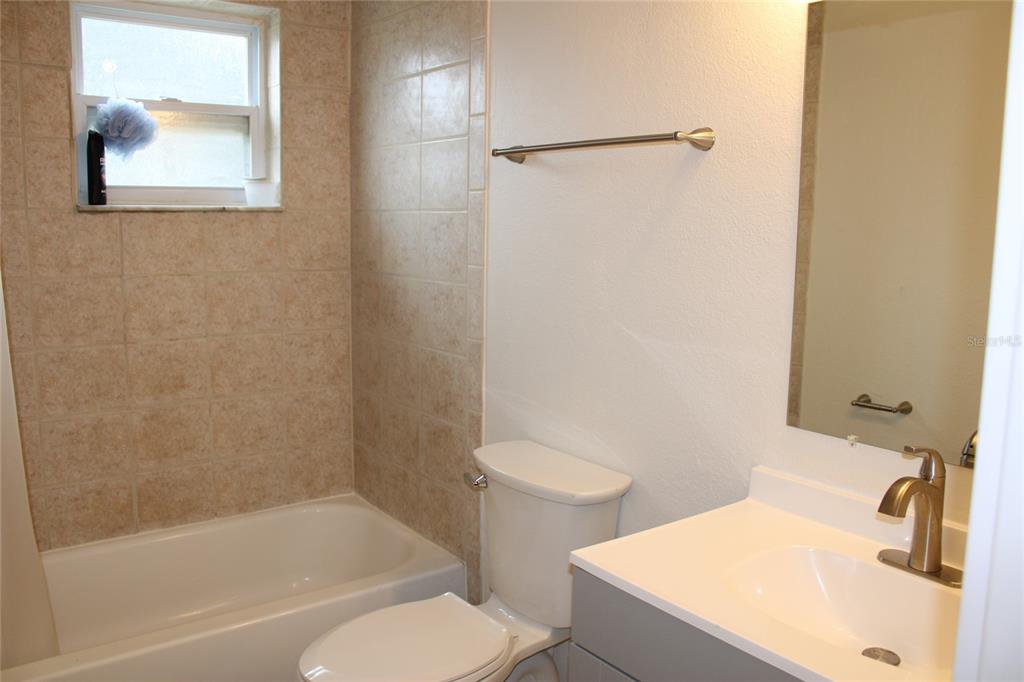 A bathroom features a tub-shower combination with beige tile, a toilet, and a vanity — 9049 ORCHID DRIVE, SEMINOLE, FL