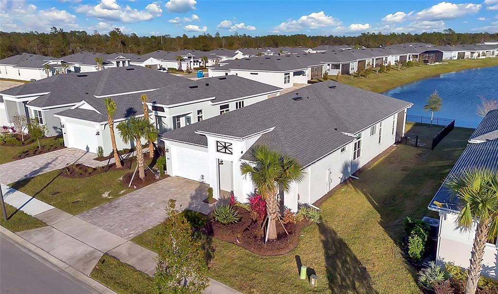 An aerial view shows suburban houses with gray roofs and white walls near a lake — 891 MEGANO BOULEVARD, DELAND, FL