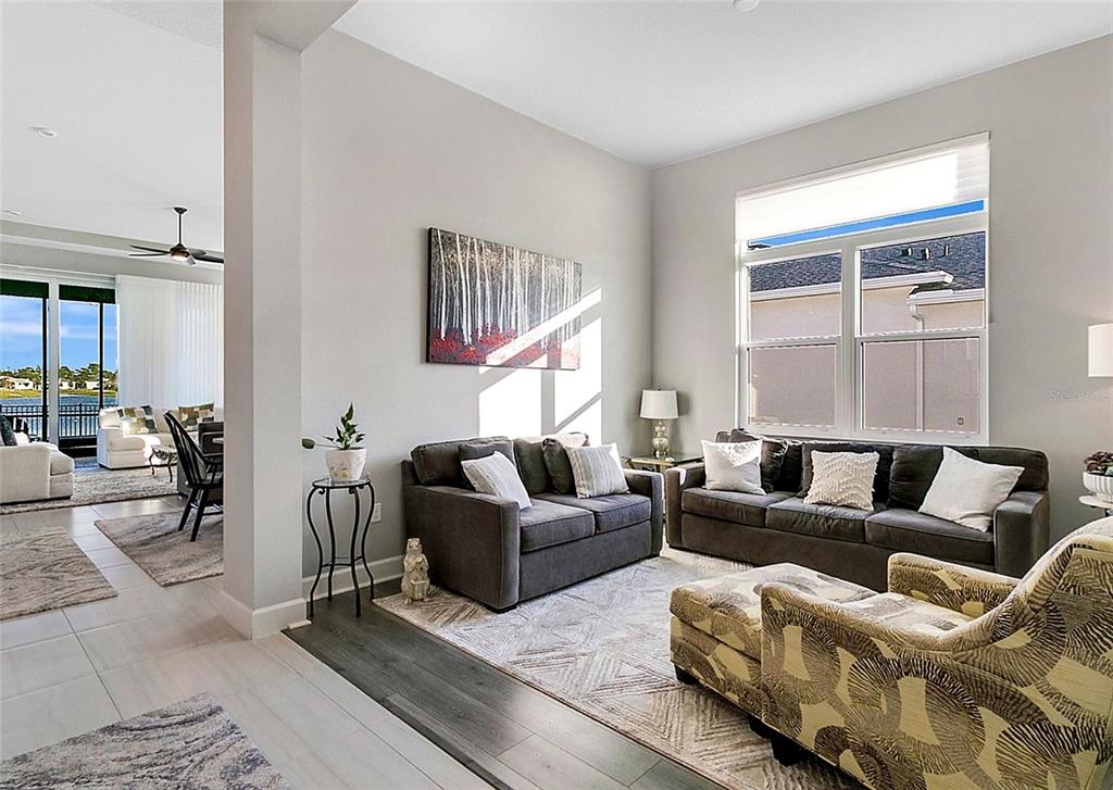 A living room features dark gray sofas, a patterned armchair, and large windows — 891 MEGANO BOULEVARD, DELAND, FL