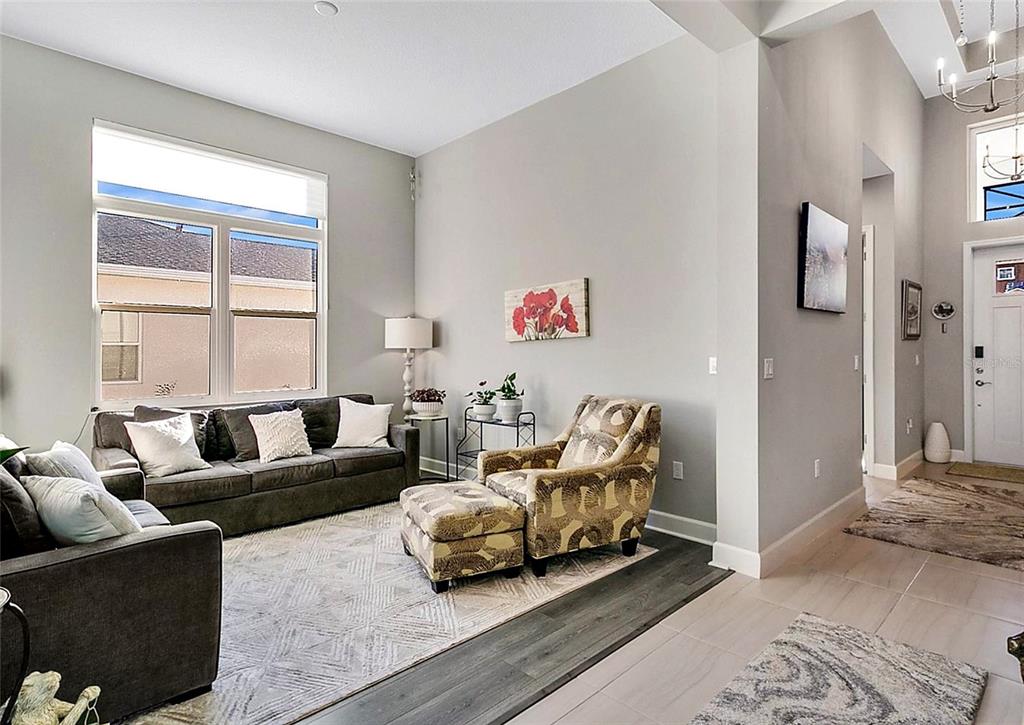 A living room features a grey sofa, patterned armchair with ottoman, and light-colored tile flooring — 891 MEGANO BOULEVARD, DELAND, FL