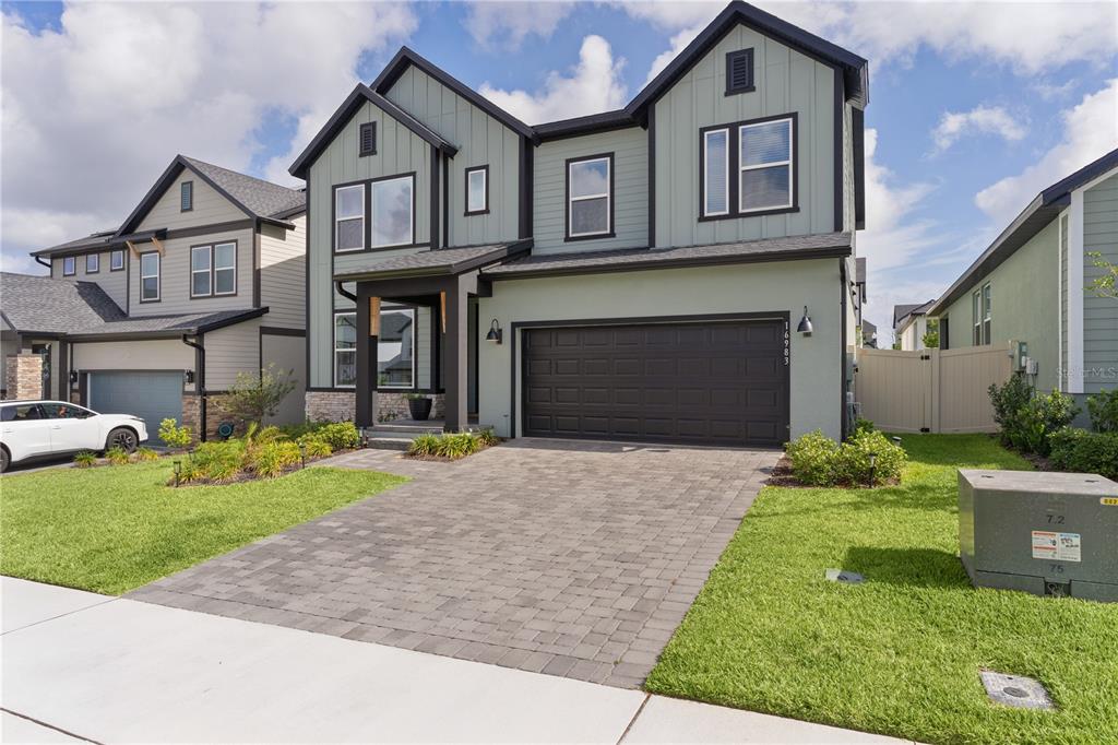 A two-story house with sage green siding, a dark garage door, and a paver driveway — 16983 CEDAR VALLEY CIRCLE, CLERMONT, FL