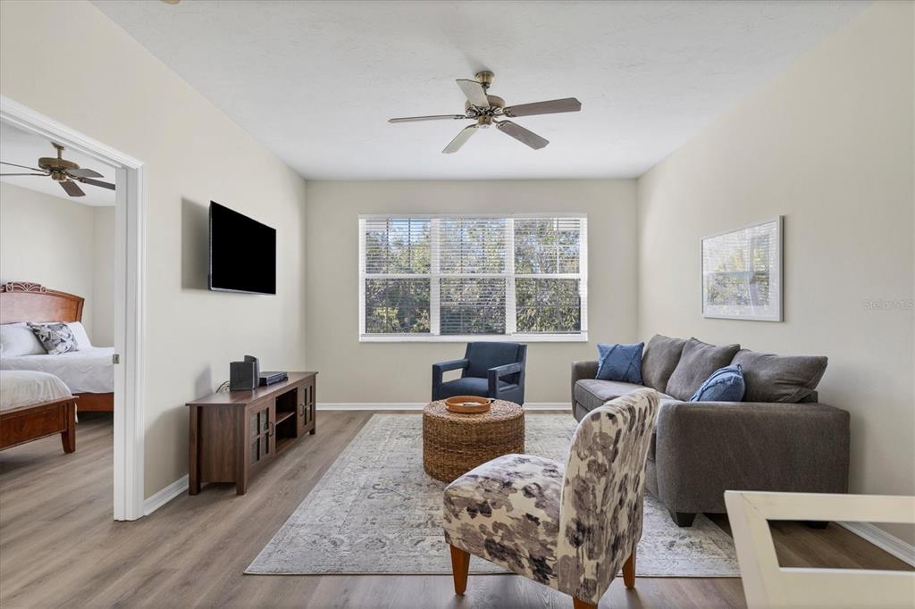 A living room features a gray sofa, patterned armchair, wood media console, and ceiling fan — 3506 54TH DRIVE W UNIT 202, BRADENTON, FL