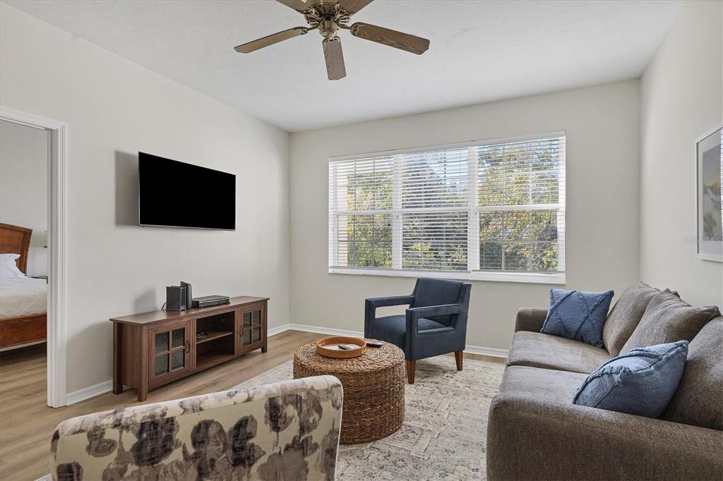 A living room features a gray sofa, a blue armchair, a television, and a ceiling fan — 3506 54TH DRIVE W UNIT 202, BRADENTON, FL