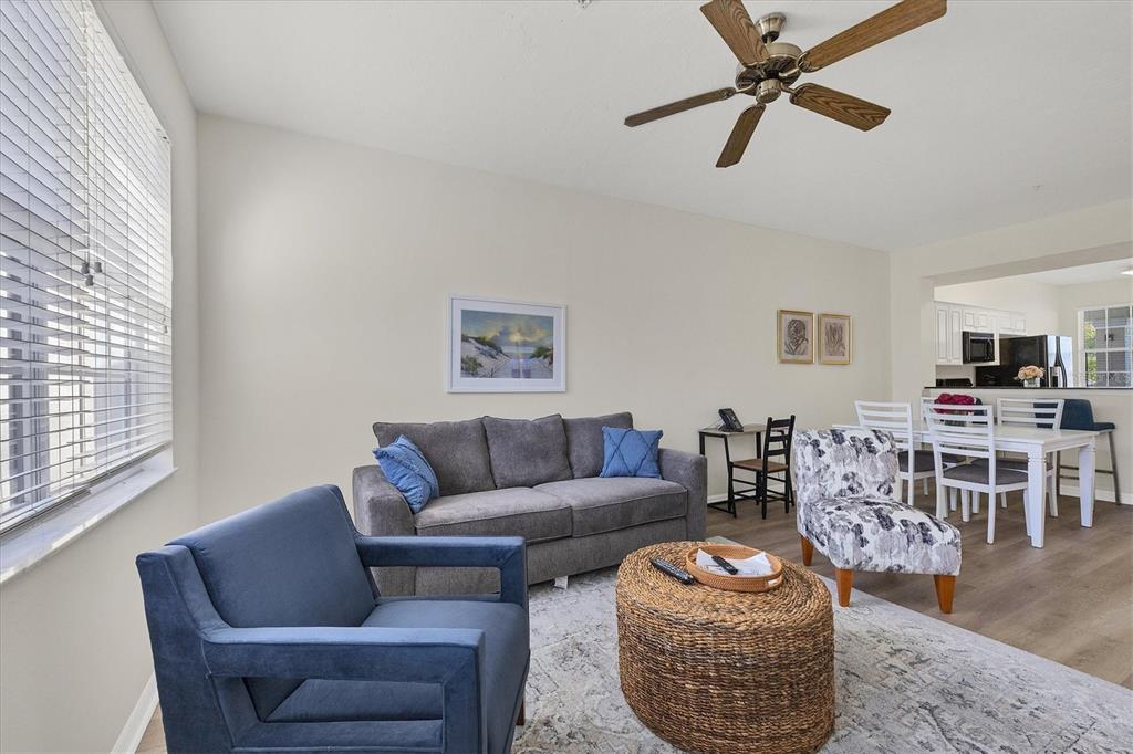 A living room features a gray sofa, a blue armchair, a woven coffee table, and dining area — 3506 54TH DRIVE W UNIT 202, BRADENTON, FL