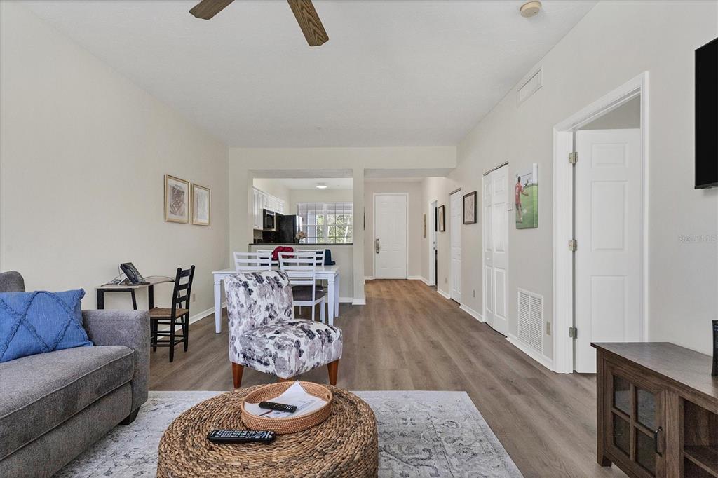 A living room with wood-look flooring, a gray sofa, and an open kitchen in the background — 3506 54TH DRIVE W UNIT 202, BRADENTON, FL