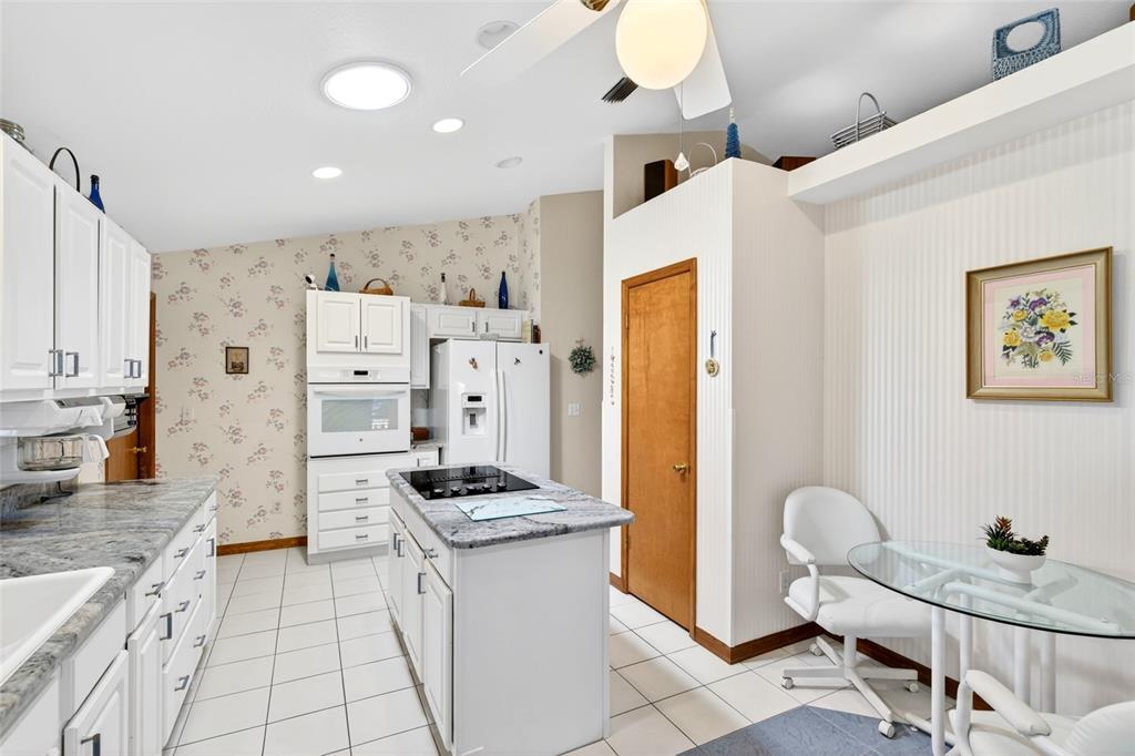 A kitchen features white cabinetry, a granite-topped island, tile flooring, and floral wallpaper — 64 BAHIA TRACE CIRCLE, OCALA, FL