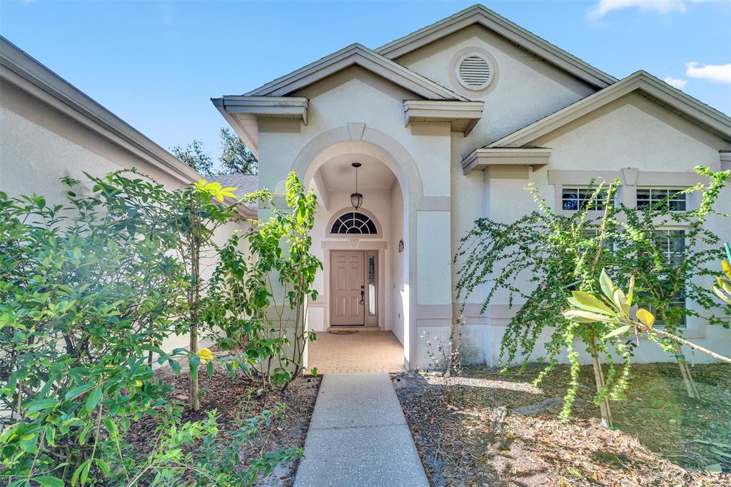 The exterior of a beige stucco house features an arched entryway and a concrete walkway — 10218 SHADOW BRANCH DRIVE, TAMPA, FL