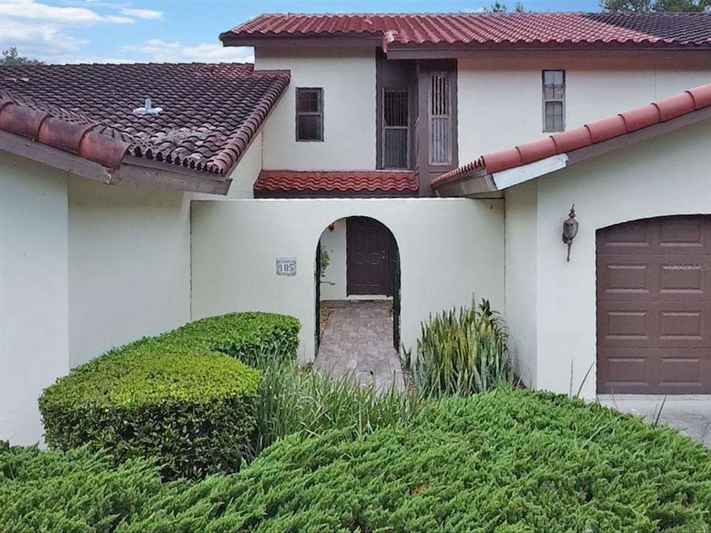 A two-story house with a tiled roof, arched entryway, and a brown garage door — 105 COVENTRY LANE, HAINES CITY, FL